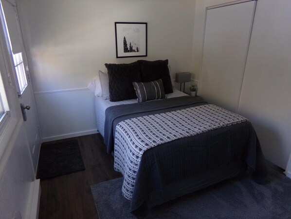 A bedroom with a bed, a bedside table with a lamp, a framed picture on the wall, and a door. - Blue River Condos 3 Bed 2 Bath (Breckenridge)
