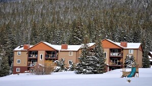 A multi-story building with balconies, surrounded by snow-covered trees and a ski slope. - Blue River Condos 3 Bed 2 Bath (Breckenridge)