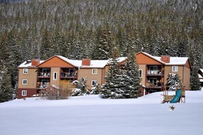 A multi-story building with balconies, surrounded by snow-covered trees and a ski slope. - Blue River Condos 3 Bed 2 Bath (Breckenridge)