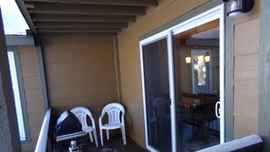 A covered outdoor area with a sliding glass door, two white plastic chairs, and a propane tank. - Blue River Condos 3 Bed 2 Bath (Breckenridge)