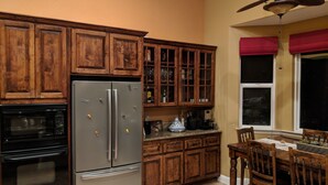 A kitchen with wooden cabinets, a stainless steel refrigerator, an oven, and a dining table with chairs. - Pokerville Retreat in the Heart of Amador Wine Country (Plymouth)
