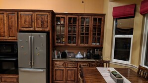 A kitchen with wooden cabinets, a stainless steel refrigerator, and a dining table with a striped tablecloth. - Pokerville Retreat in the Heart of Amador Wine Country (Plymouth)