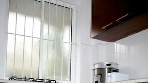 A kitchen with wooden cabinets, a window with bars, and a stove. - Bamba Flat (Colombo)