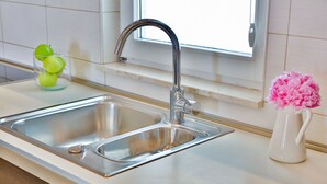 Una cocina con un lavamanos de acero inoxidable, una ventana sobre el lavamanos y un jarrón con flores rosas en la encimera.