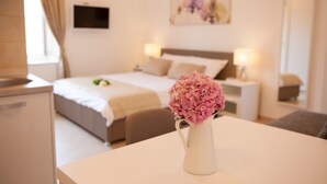 Una habitación de hotel con cama, mesitas de noche, televisor y un florero con flores sobre una mesa.