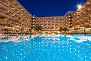 A multi-story hotel with a swimming pool, sun loungers, and umbrellas.