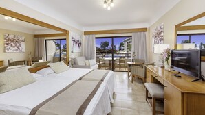 A hotel room with two beds, a desk with a TV, a balcony with a pool view, and artwork on the walls. - GF Fanabe (Costa Adeje)