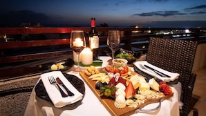 A table set for a meal with a bottle of wine, glasses, and a variety of cheeses and fruits on a wooden board. - GF Fanabe (Costa Adeje)