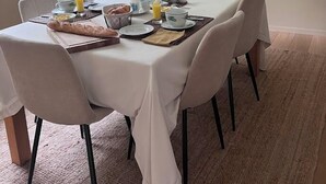 Un comedor con una mesa redonda dispuesta para el desayuno, con platos, tazones y un florero con flores.