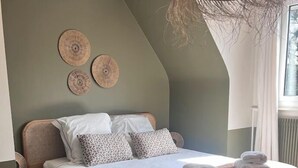 Un dormitorio con cama, mesita de noche, una silla de mimbre y una lámpara de fibras naturales.
