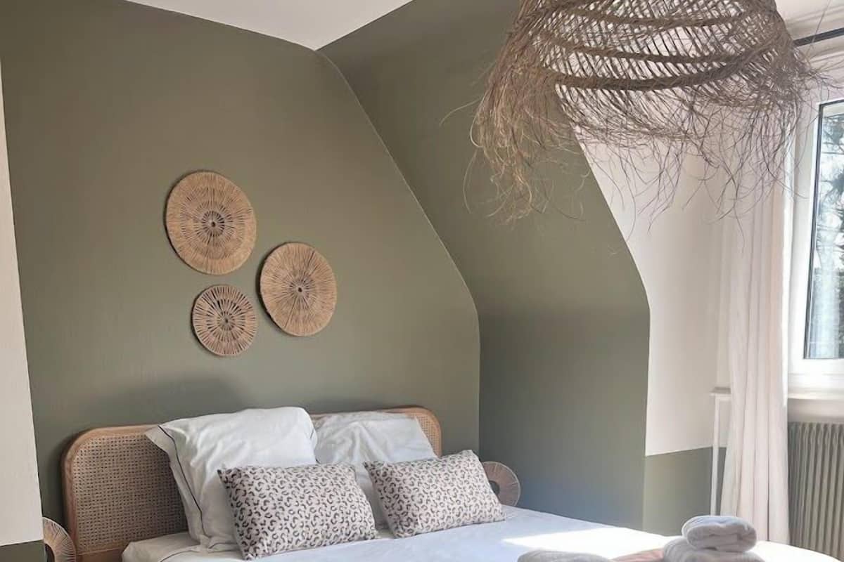 A bedroom with a bed, a bedside table, a wicker chair, and a woven light fixture.