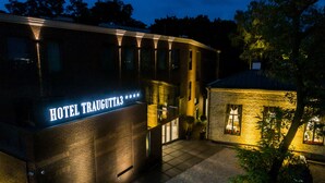 Un hotel llamado "HOTEL TRAUGUTIA" con una fachada moderna de ladrillo y letreros iluminados.