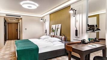 A hotel room with a bed, a desk, and a mirror. There is a door leading to another room and a window with blinds.