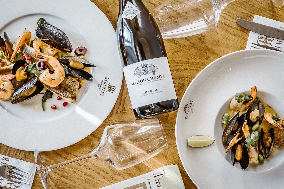 A table with two plates of seafood dishes, a bottle of wine, and a glass.