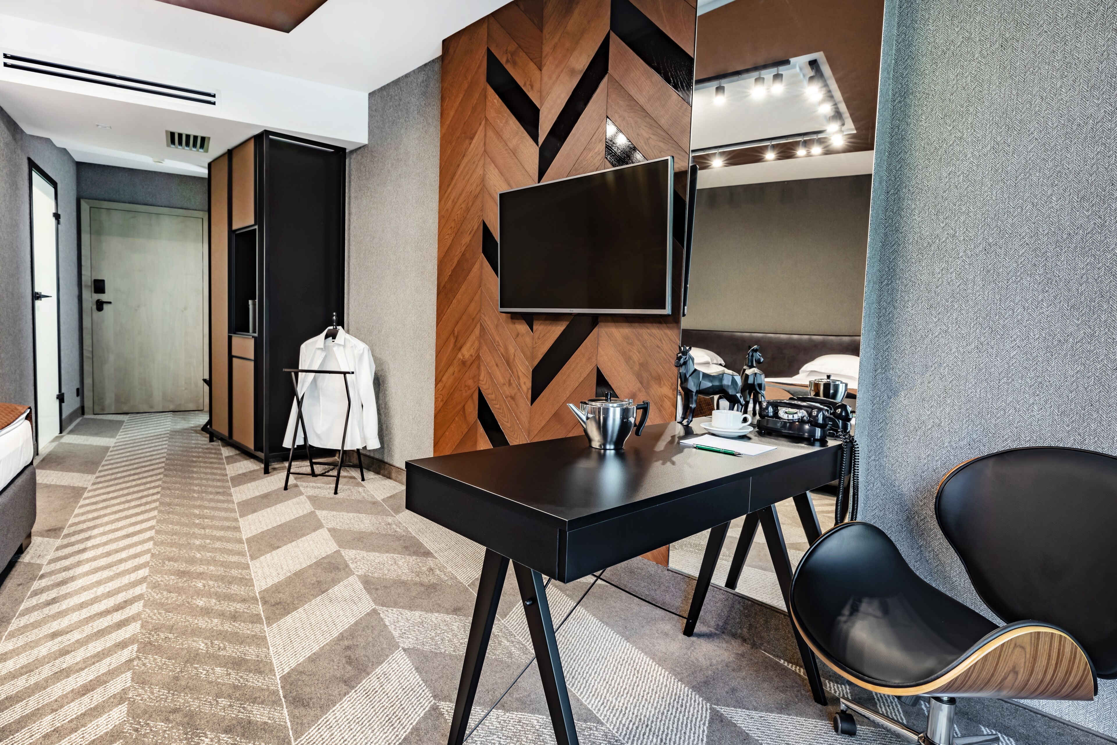 Habitación de hotel moderna con un televisor de pantalla plana grande montado en una pared de madera, un escritorio con hervidor y una zona de estar cómoda con una silla y sofá.