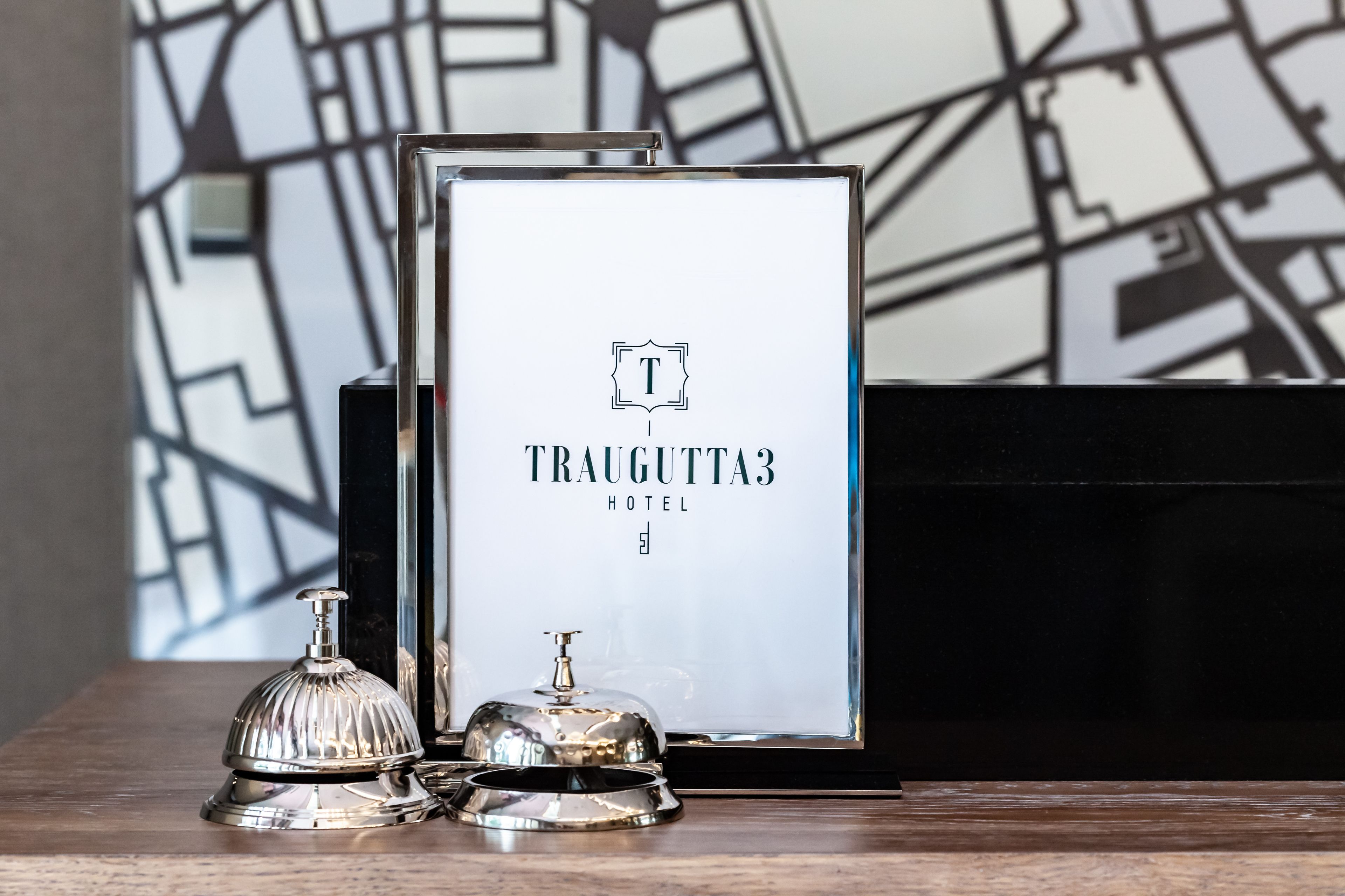 Ein gerahmtes Schild mit dem Namen 'Traugutta 3 Hotel' und einer Glocke auf einer Holzbodenfläche.