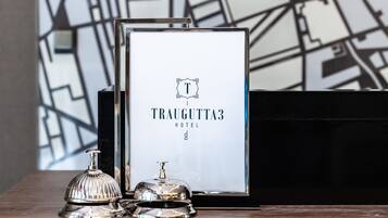 Ein gerahmtes Schild mit dem Namen 'Traugutta 3 Hotel' und einer Glocke auf einer Holzbodenfläche.