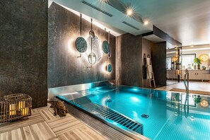 Une piscine intérieure moderne, avec une eau cristalline, un plancher en bois et un mur en pierre orné de miroirs ronds.