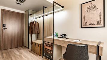 Una habitación moderna con suelo de madera, un escritorio con teléfono y botellas, un perchero y un certificado enmarcado en la pared.