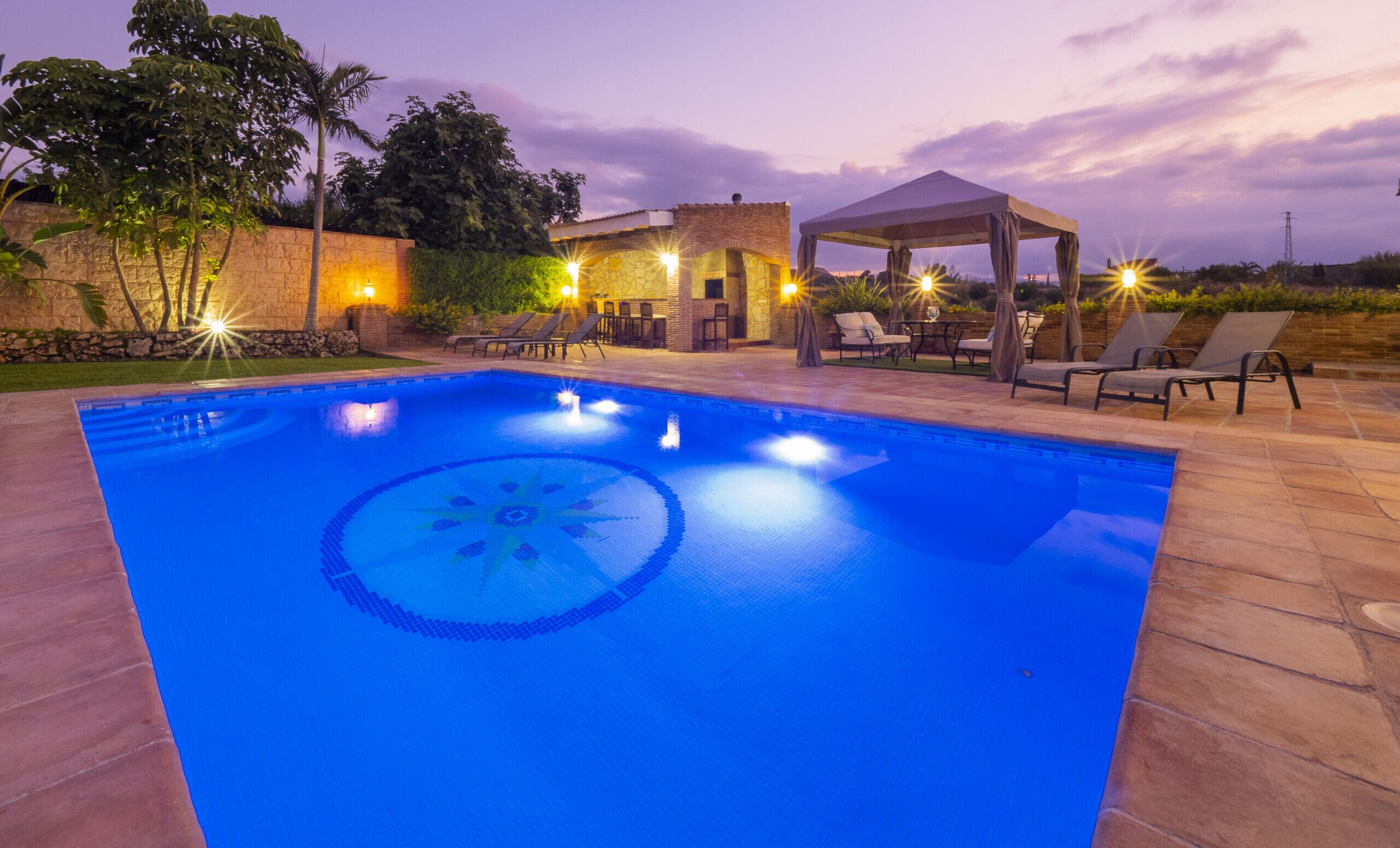 A swimming pool with a geometric pattern, surrounded by lounge chairs and a covered seating area.