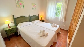 A double room with two beds, a nightstand with a lamp, and a window with curtains.