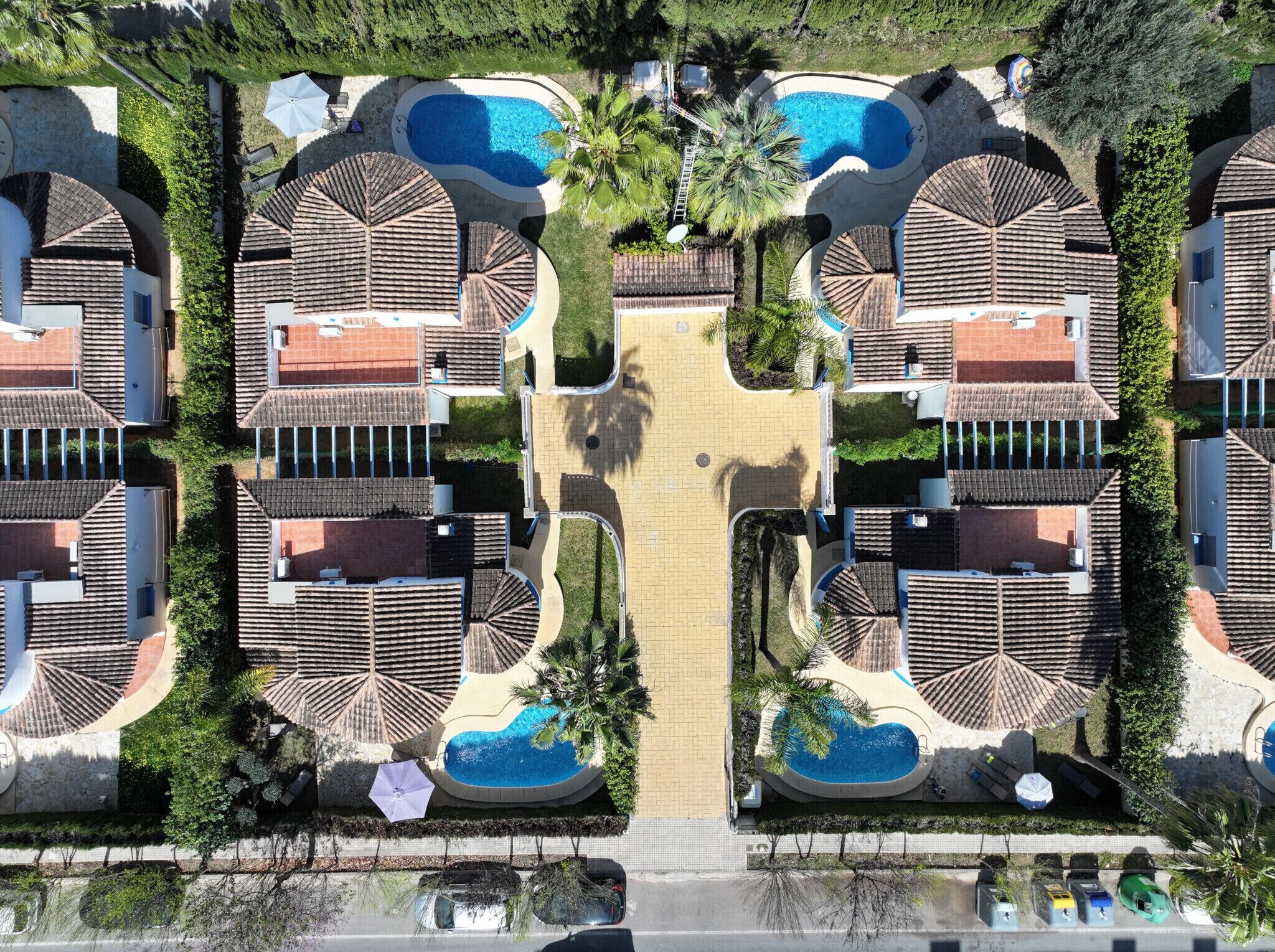 Eine Vogelperspektive zeigt ein Resort mit mehreren Villen, jede mit einem Schwimmbad, umgeben von Palmen und einem zentralen Gang.