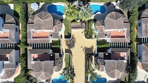 Oversigtsbillede af et resort med flere villaer, hver med egen swimmingpool, omgivet af palmer og en central gangsti.