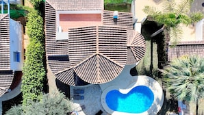 Et hus med et unikt tagdesign, en swimmingpool og frodig vegetation.
