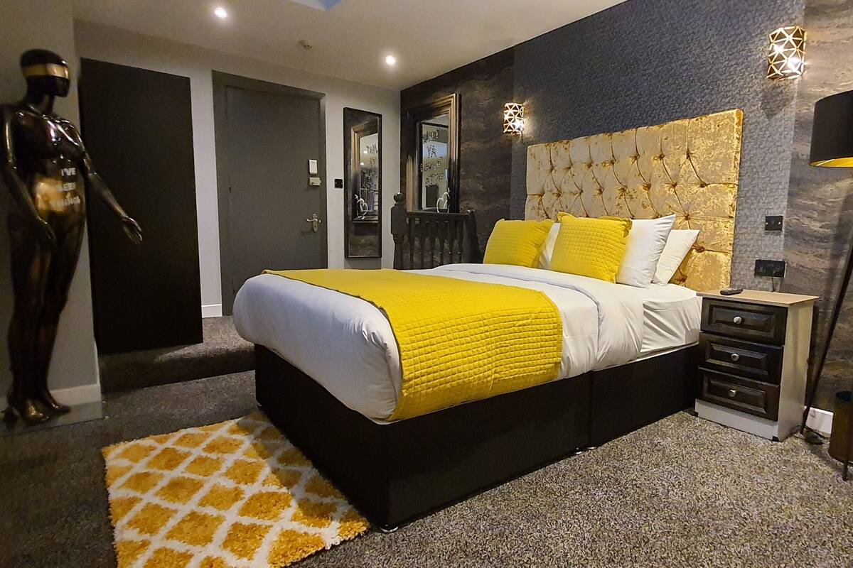 Un dormitorio con cama, mesitas de noche, lámpara, un maniquí y un espejo.