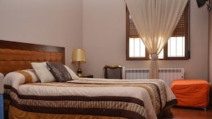 A bedroom with a bed, a nightstand, a lamp, a window with curtains, and a radiator. - La Barraca de Culón (Cañada Juncosa)