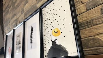 Een muur met ingelijste kunstwerken, waaronder een veer, een silhouet met een hoed en een tekst.