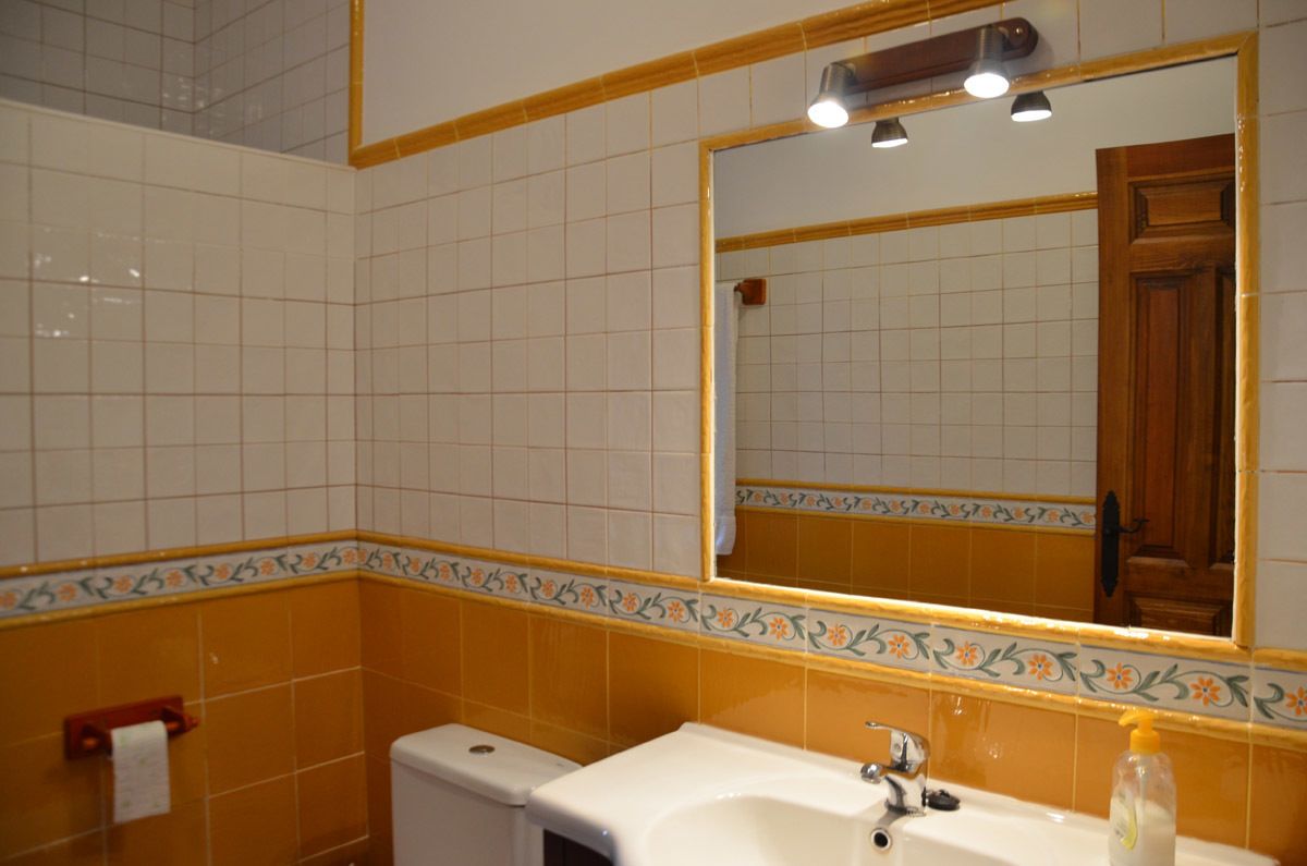 Un baño con azulejos blancos, un borde decorativo amarillo, un lavabo, un espejo y un inodoro.