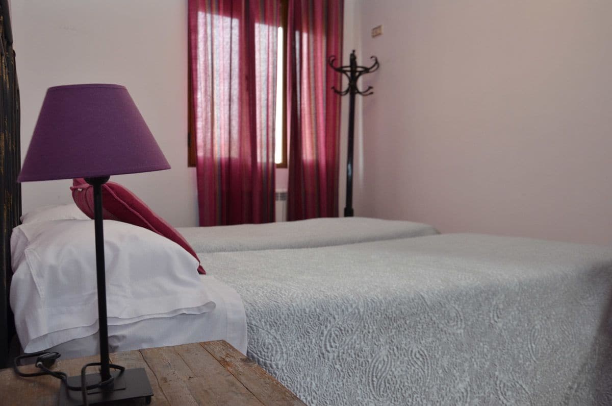 A room with two beds, a lamp, and a coat rack.