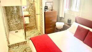 A hotel room with a bed, a shower, a dresser, and a window.
