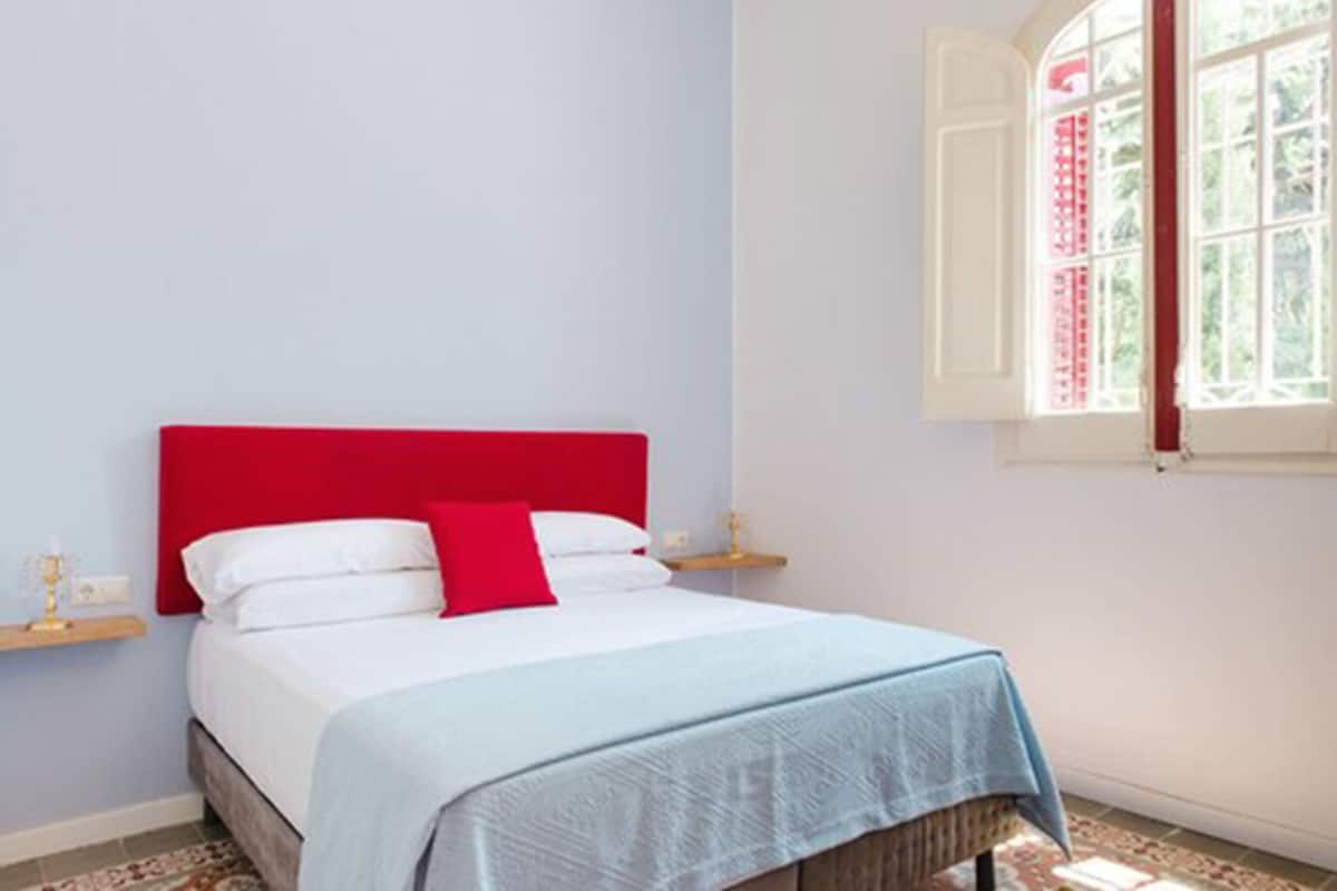 A bedroom with a red headboard, white bedding, and a blue bedspread.