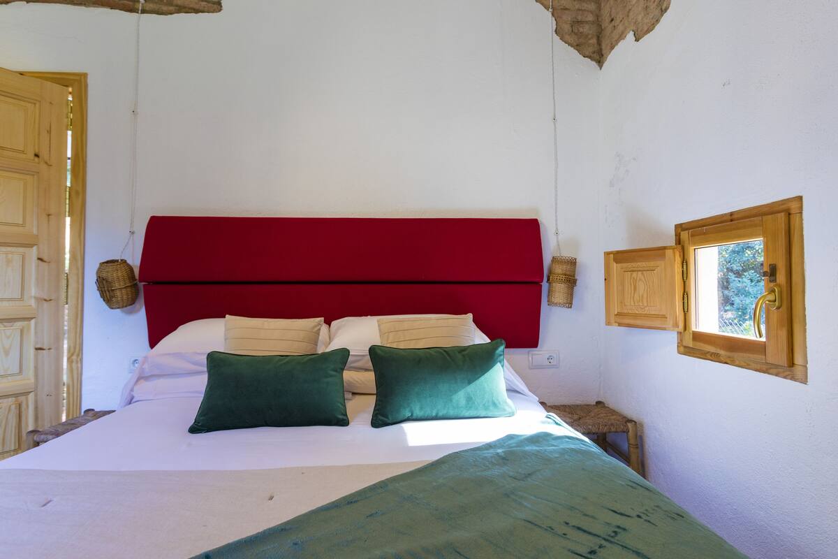 A bed with a red headboard, two green pillows, and a white bedspread.
