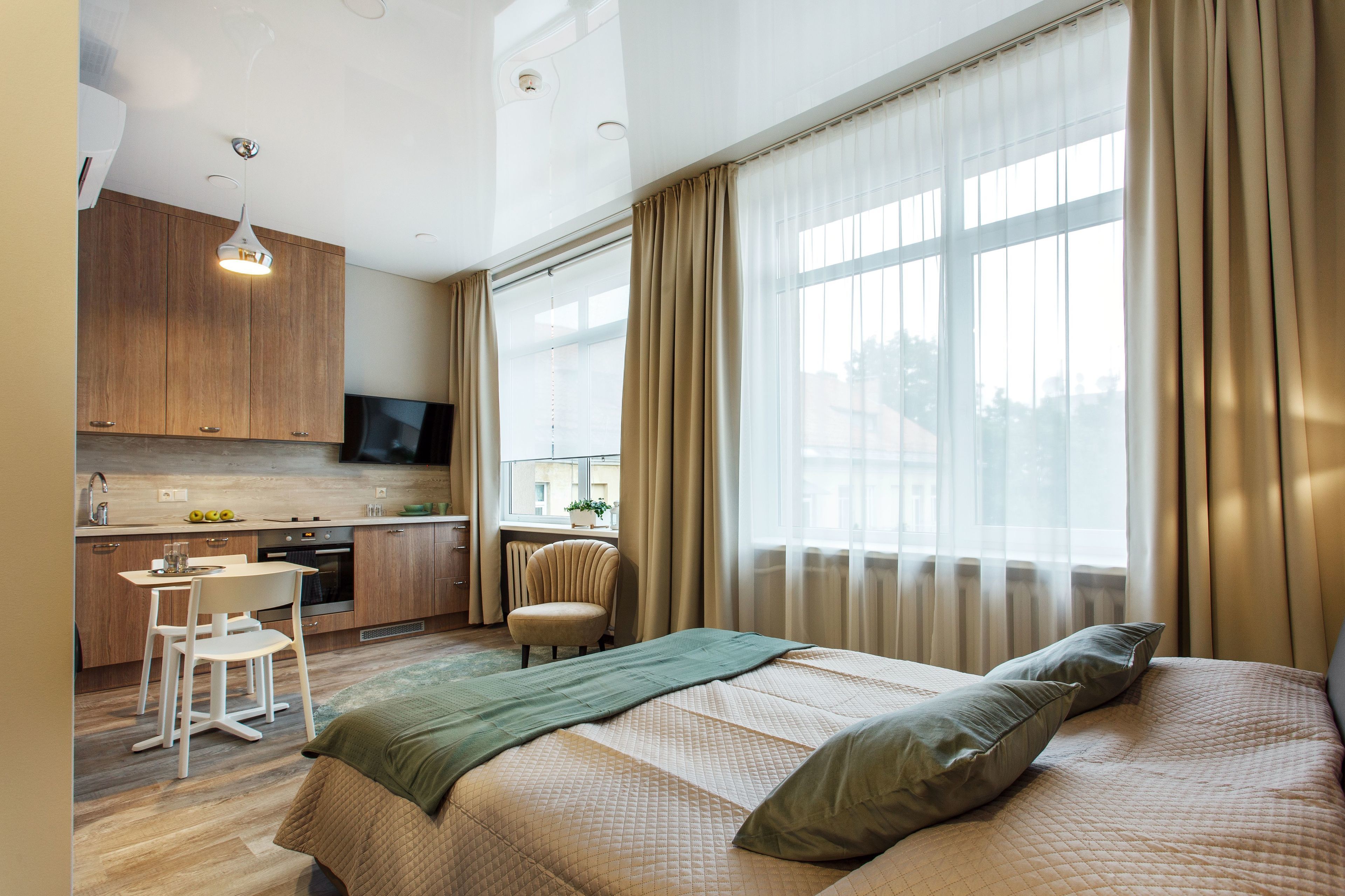 A modern hotel room with a large bed, a desk, and a kitchenette.