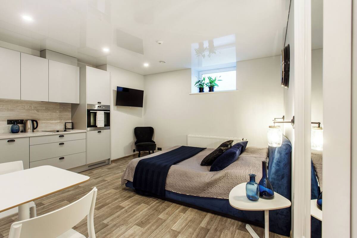A modern bedroom with a bed, bedside table, and a window with plants.