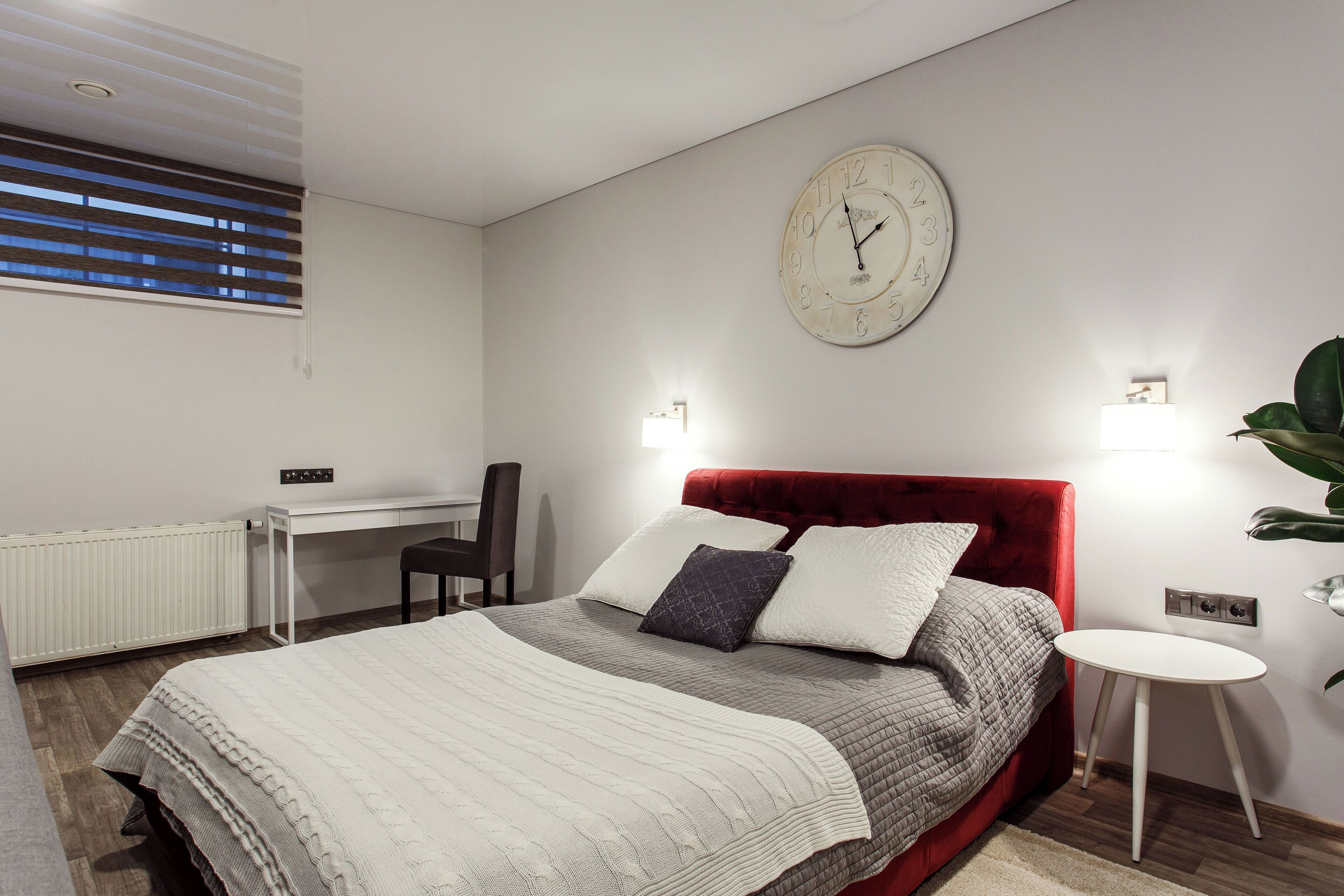 A modern bedroom with a bed, a desk, and a red headboard.
