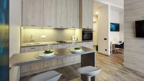 A modern kitchen with wooden cabinets, a central island with bar stools, and a dining area with a black chair. - Old Town Trio Apartments (Vilnius)