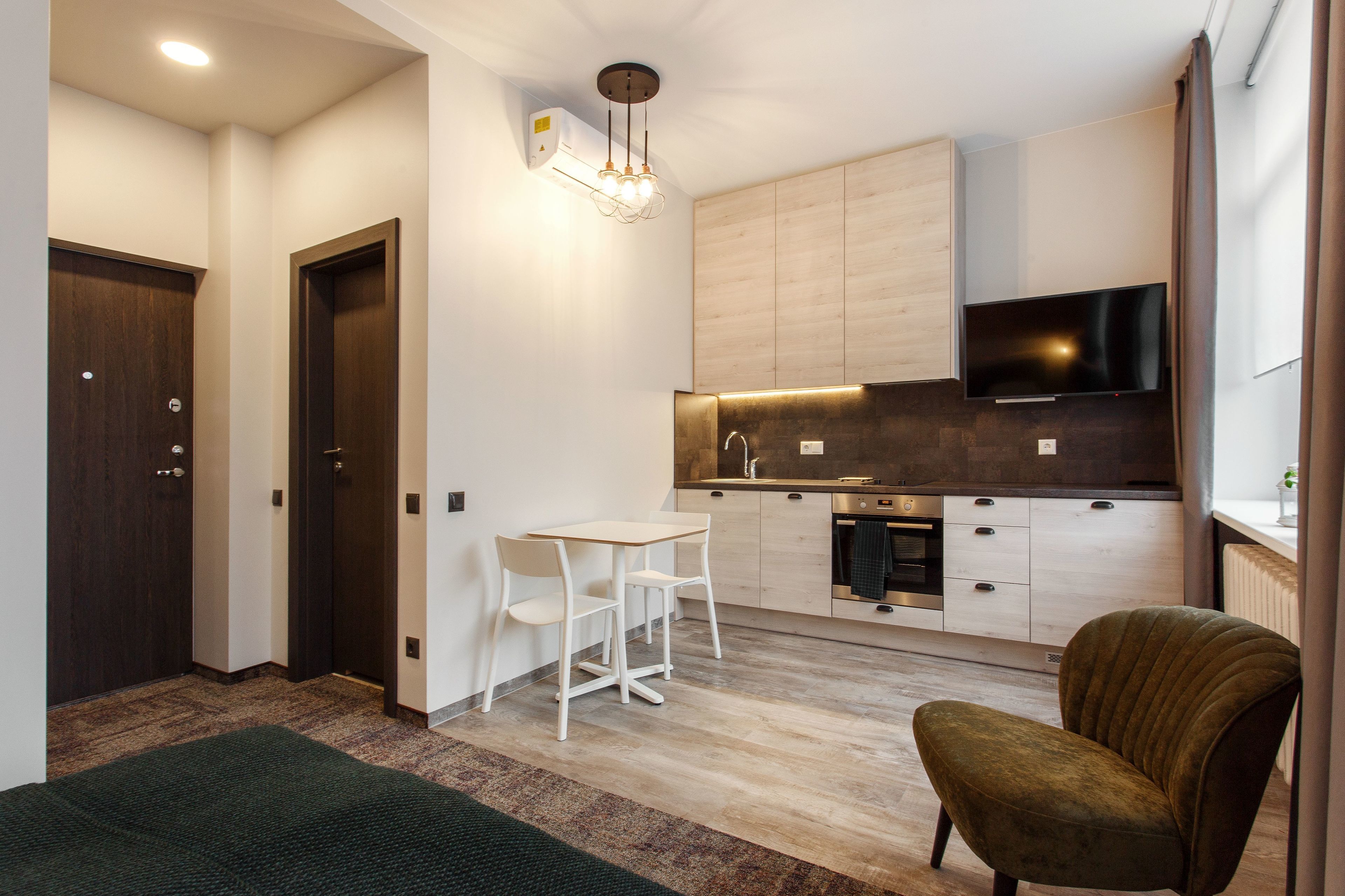 Una cocina moderna con televisor de pantalla plana, armarios de madera y una zona de comedor con sillas blancas.
