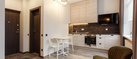 Una cocina moderna con televisor de pantalla plana, armarios de madera y una zona de comedor con sillas blancas.