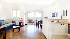 Un salón luminoso con un sofá azul, una mesa de centro de madera y vista al mar a través de un ventanal.