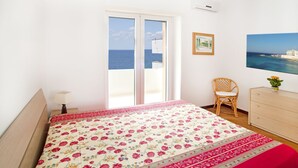 Un dormitorio con cama, una silla, un aparador y vista al mar a través de un ventanal corredera.