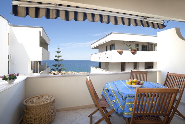 A balcony with a table set for dining, overlooking a beach and a clear blue sky.