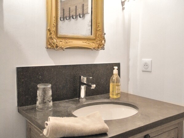A bathroom with a marble sink, a glass jar, a towel, a bottle of hand soap, and a gold-framed mirror.
