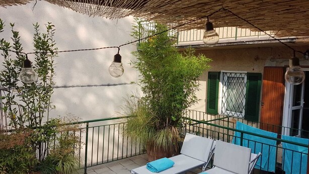 A balcony with two white lounge chairs, a potted plant, and a hanging light fixture.
