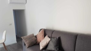A modern living room with a grey sofa, a white chair, and a wall-mounted air conditioner.