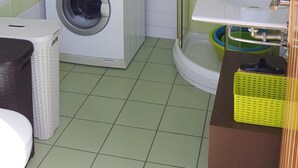 A compact laundry room with a stacked washer and dryer, a glass shower enclosure, and a sink with a green basket. - Luxury Loft in Gran Canaria. Jacuzzi and Free WIFI. (Sta Brígida)