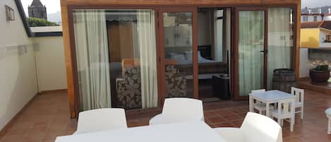 A patio with a table and chairs, a sliding glass door leading to a bedroom, and a view of a mountain in the background.